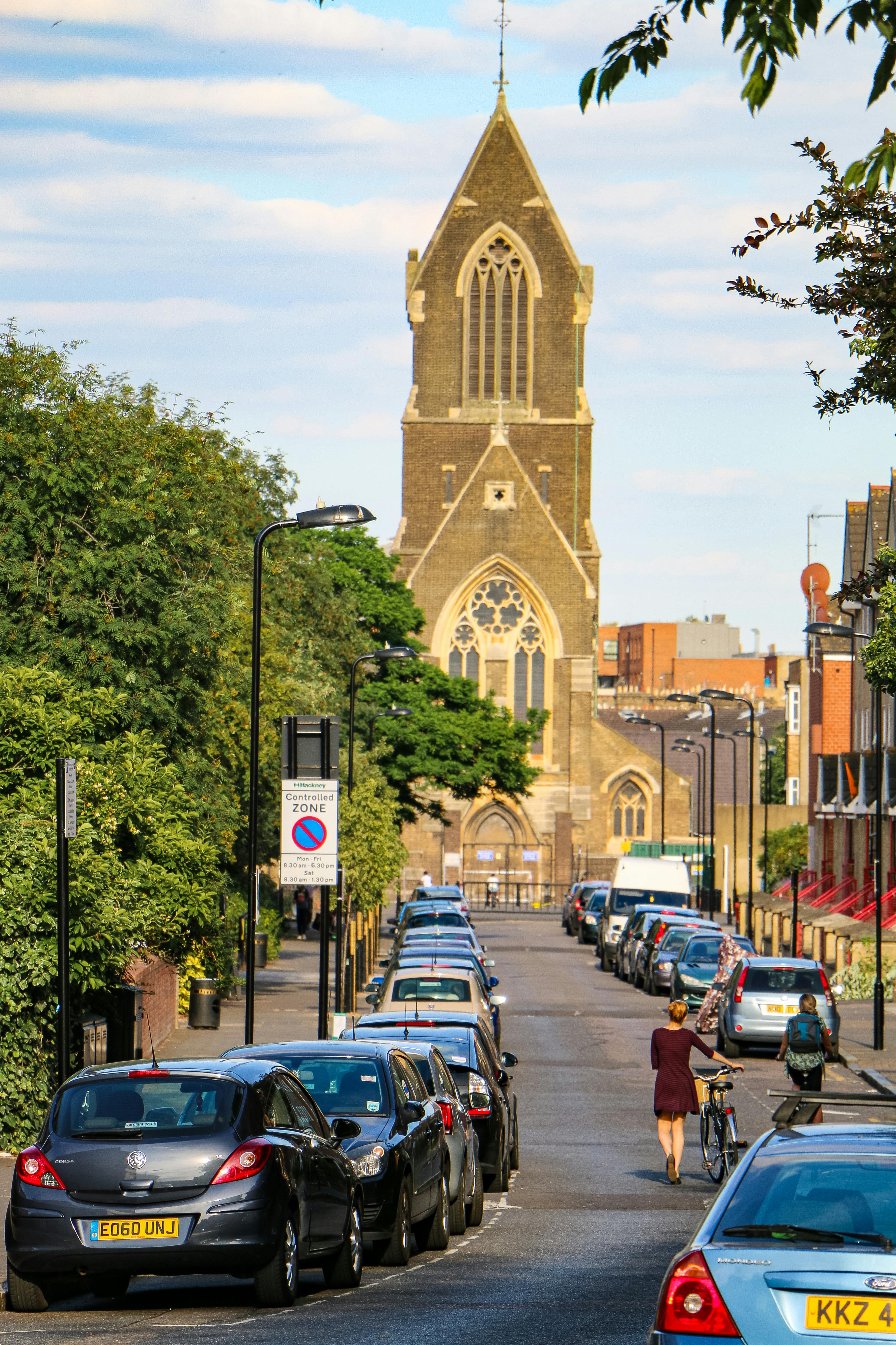 Residential street with parked cars, cyclist, and historic church in background